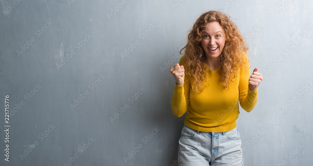 Fototapeta premium Young redhead woman over grey grunge wall screaming proud and celebrating victory and success very excited, cheering emotion