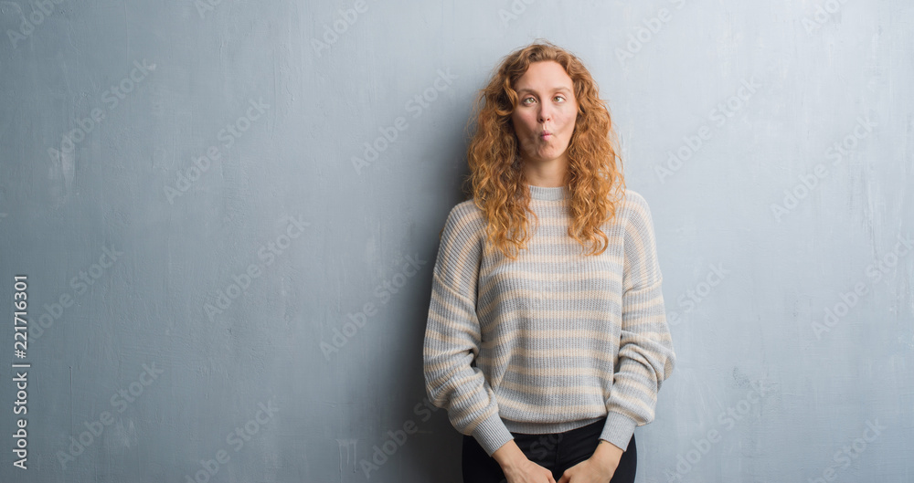 Young redhead woman over grey grunge wall making fish face with lips, crazy and comical gesture. Funny expression. Young redhead woman over grey grunge wall making fish face with lips, crazy and comical gesture. Funny expression.