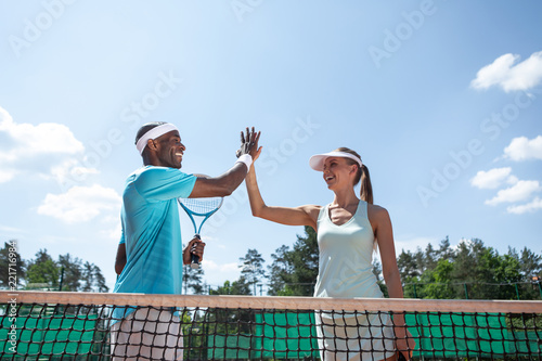 Low angle of happy man and woman standing near net during match in open air. They are giving high-five while celebrating good results. Team sport games for health and pleasure concept photo