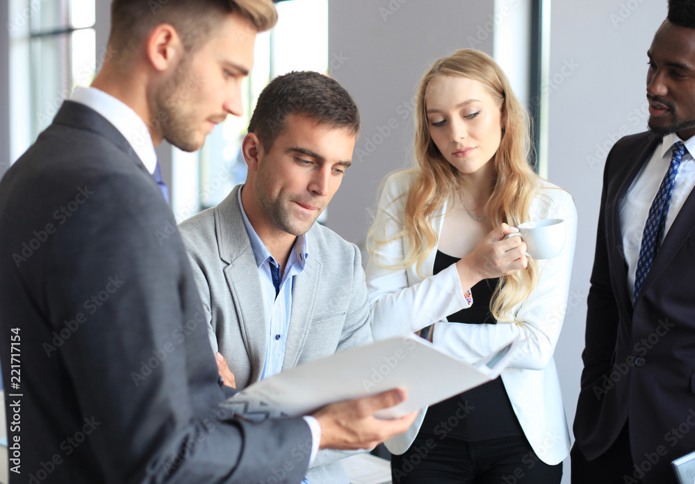 Young modern colleagues in smart casual wear having a brainstorm meeting while standing in the creative office. Young modern colleagues in smart casual wear having a brainstorm meeting while standing in the creative office.
