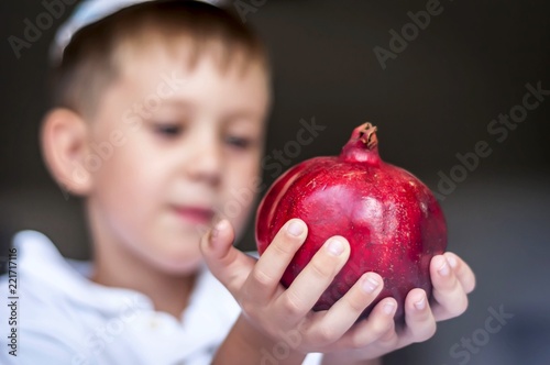 Cute Caucasian kid holding a ripe pomegranate fruit in his hands. Rosh Hashanah, Jewish New Year holiday concept image.