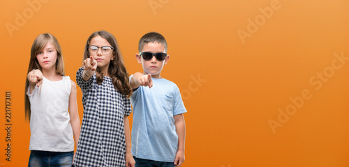 Group of boy and girls kids over orange background pointing with finger to the camera and to you, hand sign, positive and confident gesture from the front
