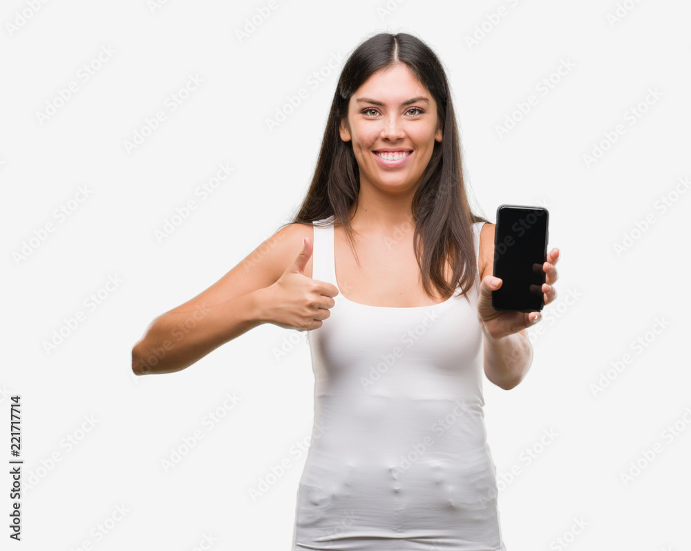 Young beautiful hispanic showing smartphone happy with big smile doing ok sign, thumb up with fingers, excellent sign Young beautiful hispanic showing smartphone happy with big smile doing ok sign, thumb up with fingers, excellent sign