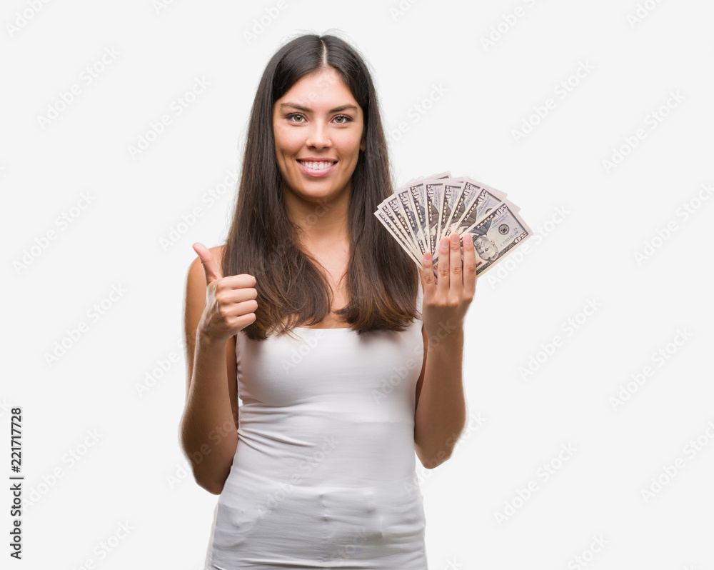 Young hispanic woman holding dollars happy with big smile doing ok sign, thumb up with fingers, excellent sign Young hispanic woman holding dollars happy with big smile doing ok sign, thumb up with fingers, excellent sign