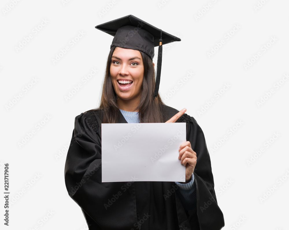 Young hispanic woman wearing graduated uniform holding diploma paper very happy pointing with hand and finger to the side Young hispanic woman wearing graduated uniform holding diploma paper very happy pointing with hand and finger to the side