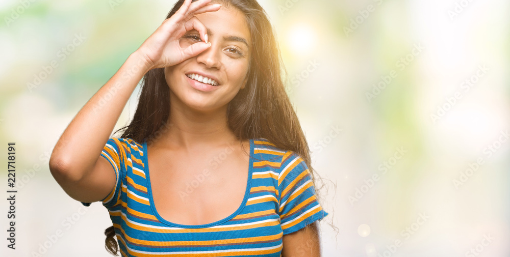 Young beautiful arab woman over isolated background doing ok gesture with hand smiling, eye looking through fingers with happy face. Young beautiful arab woman over isolated background doing ok gesture with hand smiling, eye looking through fingers with happy face.