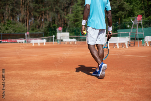 Player is having tennis set among green nature. He is standing with focus on back and using racket and ball. Copy space in left side