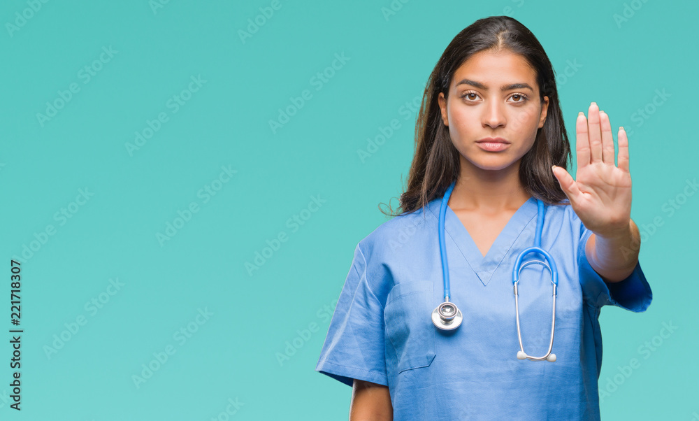 Young arab doctor surgeon woman over isolated background doing stop sing with palm of the hand. Warning expression with negative and serious gesture on the face.