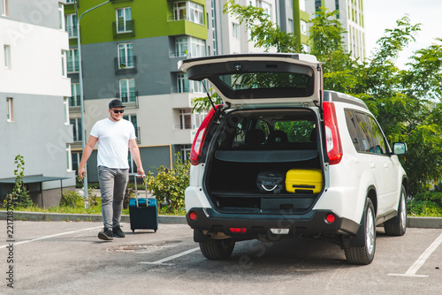 man pull suitcase with wheels to car trunk
