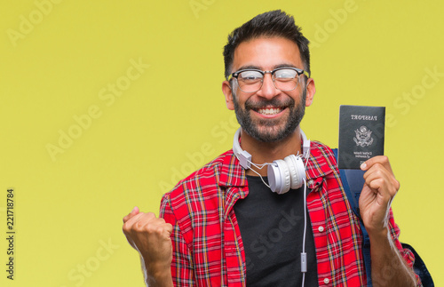 Adult hispanic student man holding passport of america over isolated background screaming proud and celebrating victory and success very excited, cheering emotion © Krakenimages.com