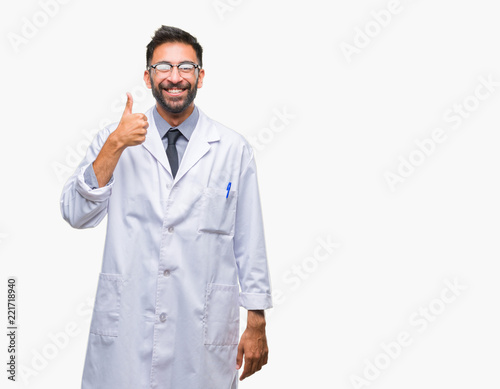Adult hispanic scientist or doctor man wearing white coat over isolated background doing happy thumbs up gesture with hand. Approving expression looking at the camera with showing success.