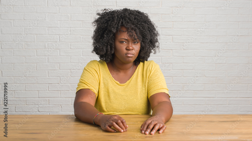 Fototapeta premium Young african american woman sitting on the table at home skeptic and nervous, frowning upset because of problem. Negative person.