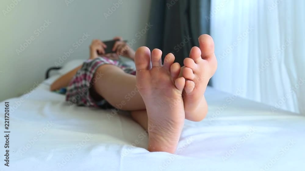 Closeup view video of cute happy young kid of school age playing computer games using modern black smartphone while laying in bed in morning. Focus at two white male preteen barefoot feet.  Stock ビデオ | Adobe Stock 