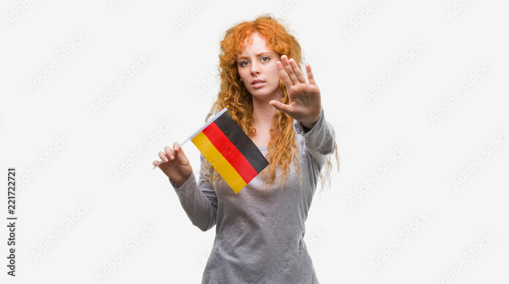 Young redhead woman holding flag of Germany with open hand doing stop sign with serious and confident expression, defense gesture Young redhead woman holding flag of Germany with open hand doing stop sign with serious and confident expression, defense gesture