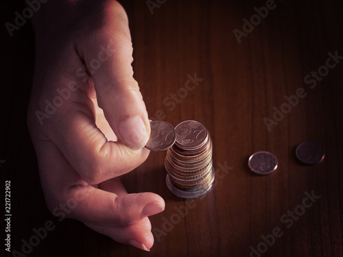Mature, woman hand putting coins into a pile, heap, on white tablecloth background. Close. European euro coins, counting pennies, small change. Note filtered image to focus on the coins.