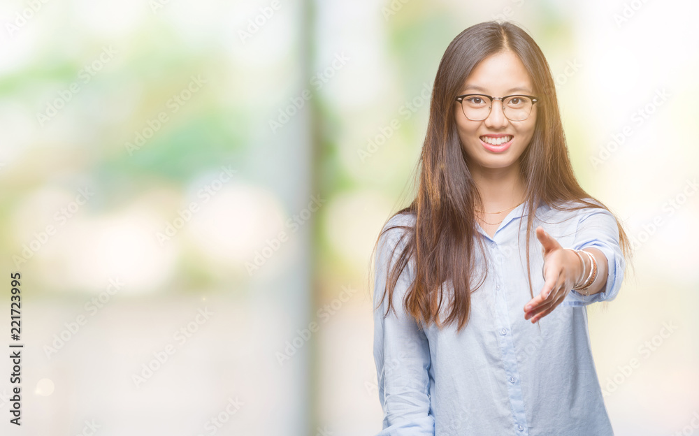 Young asian business woman wearing glasses over isolated background smiling friendly offering handshake as greeting and welcoming. Successful business. Young asian business woman wearing glasses over isolated background smiling friendly offering handshake as greeting and welcoming. Successful business.