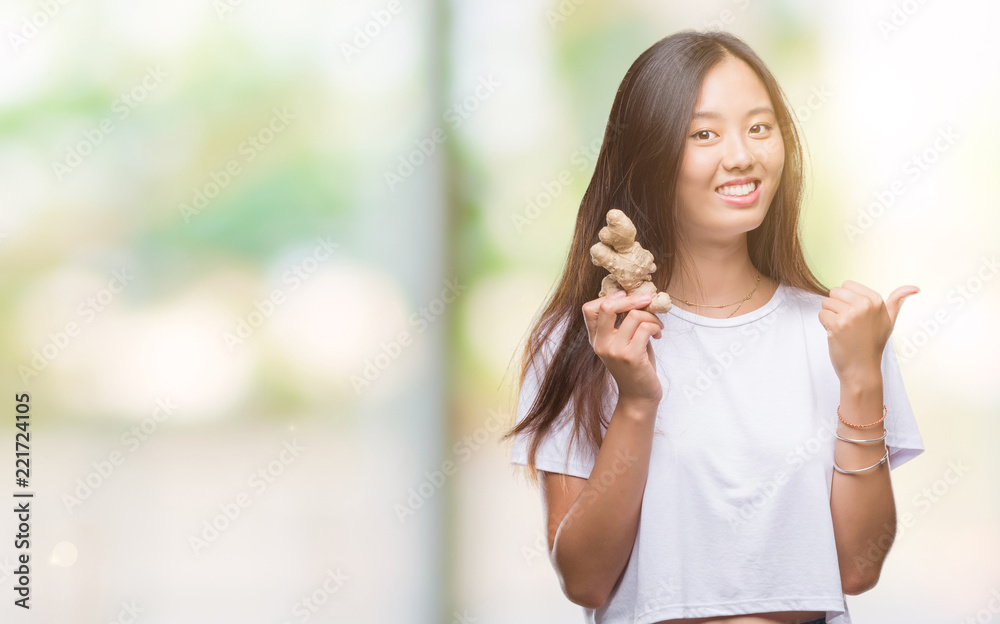 Young asian woman holding fresh organic over isolated background pointing and showing with thumb up to the side with happy face smiling