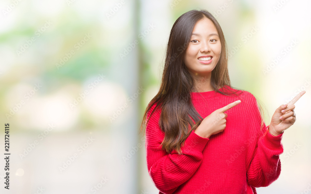 Young asian woman wearing winter sweater over isolated background smiling and looking at the camera pointing with two hands and fingers to the side.