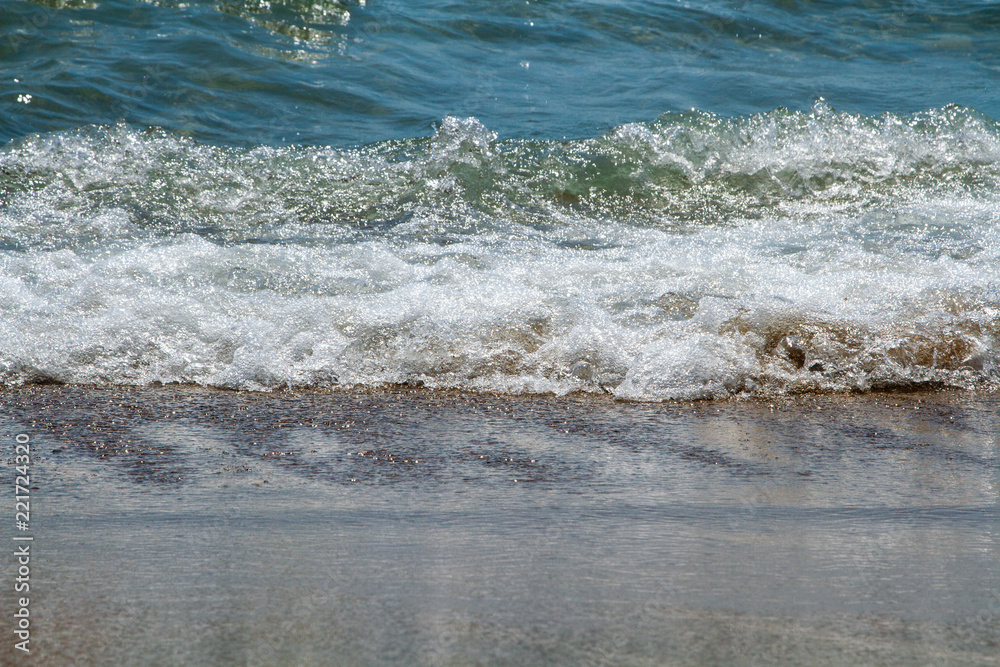 Small waves roll on the sandy shore on a bright sunny day. Pure sea and easy surf on a calm clear day. Small waves roll on the sandy shore on a bright sunny day. Pure sea and easy surf on a calm clear day.