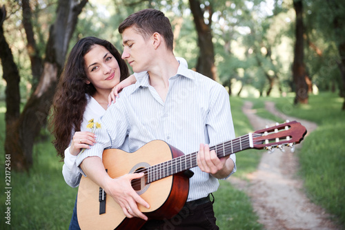young couple walking in the forest and playing guitar, summer nature, bright sunlight, shadows and green leaves, romantic feelings © soleg