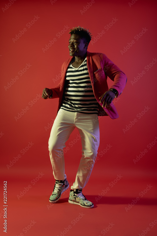 Feeling happy. Full length portrait of smiling guy in stylish clothes moving to the rhythm of music. Isolated on red background
