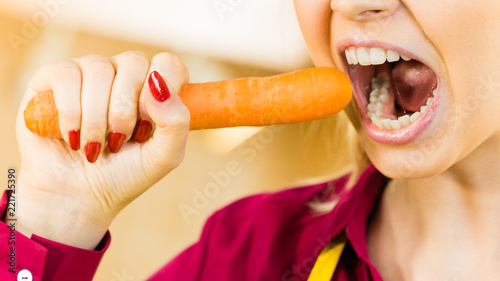 Woman holding biting carrot.