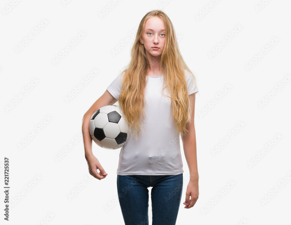 Blonde teenager woman holding soccer football ball with a confident expression on smart face thinking serious