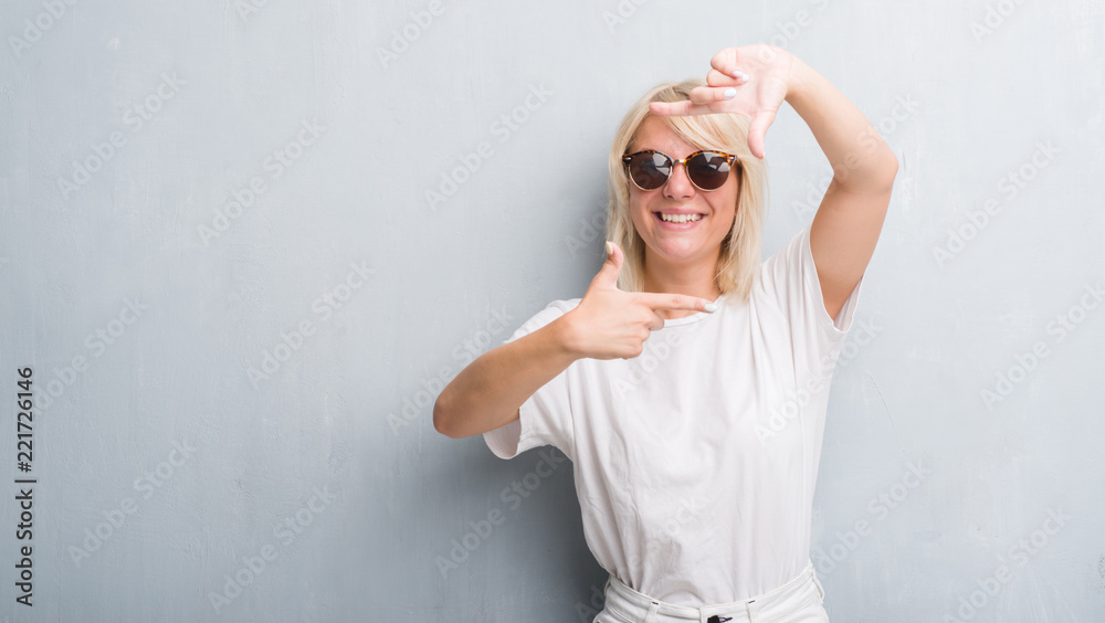 Adult caucasian woman over grunge grey wall wearing sunglasses smiling making frame with hands and fingers with happy face. Creativity and photography concept. Adult caucasian woman over grunge grey wall wearing sunglasses smiling making frame with hands and fingers with happy face. Creativity and photography concept.