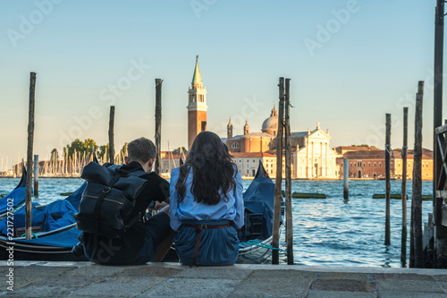 couple of tourists are sitting by the canal with gondolas in Venice, Italy © k_samurkas