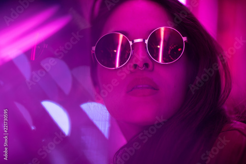 Long hair girl with sunglasses and leather jacket looking at neon lights