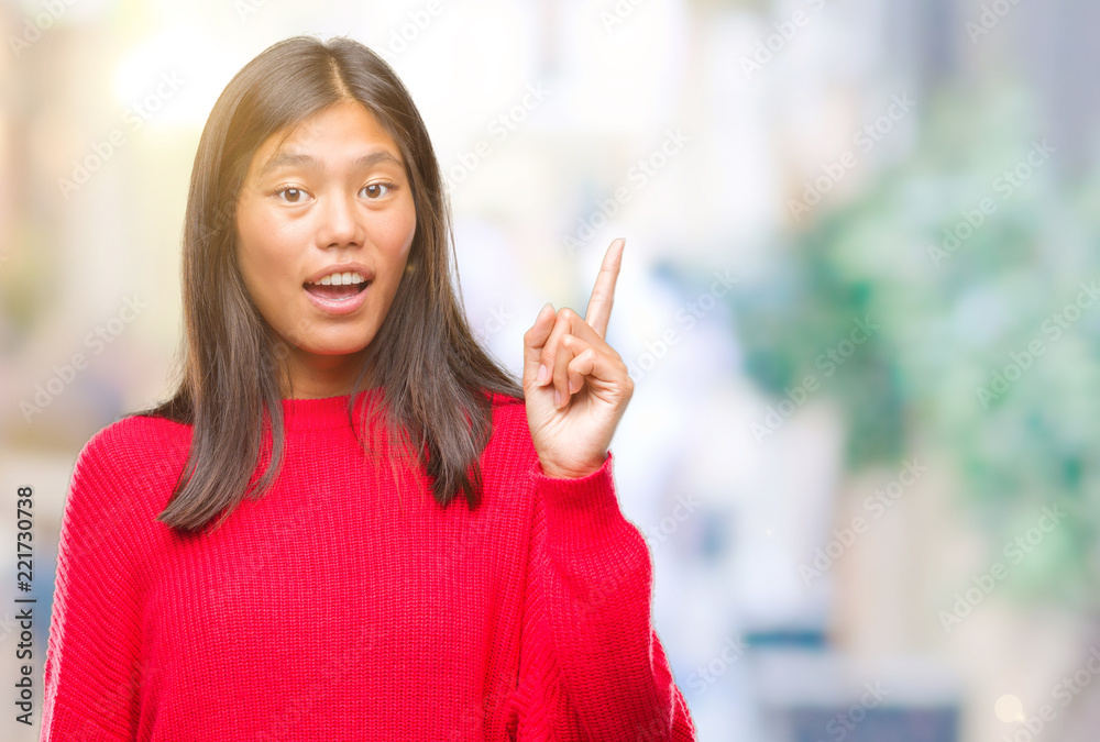 Young asian woman wearing winter sweater over isolated background pointing finger up with successful idea. Exited and happy. Number one.