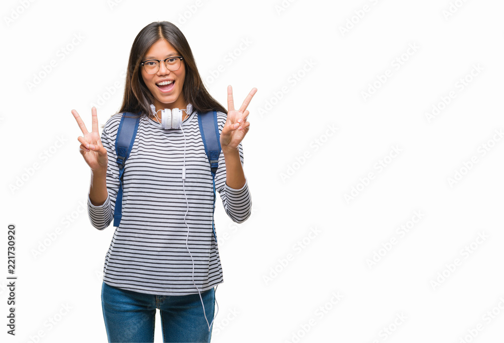 Young asian student woman wearing headphones and backpack over isolated background smiling with happy face winking at the camera doing victory sign. Number two. Young asian student woman wearing headphones and backpack over isolated background smiling with happy face winking at the camera doing victory sign. Number two.