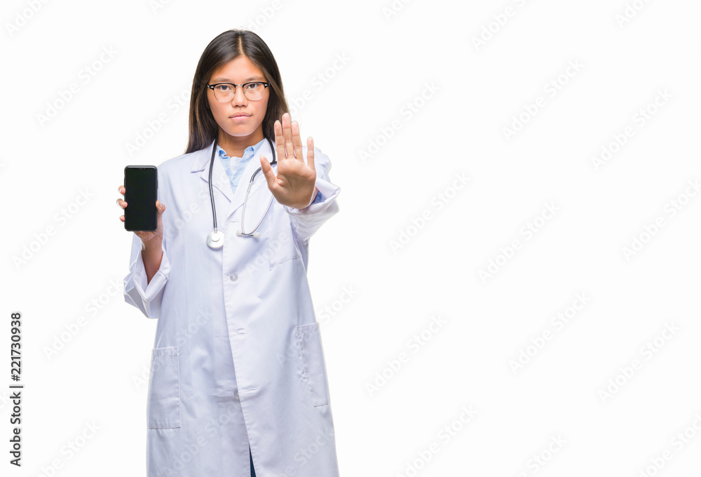 Young asian doctor woman holding smartphone over isolated background with open hand doing stop sign with serious and confident expression, defense gesture Young asian doctor woman holding smartphone over isolated background with open hand doing stop sign with serious and confident expression, defense gesture