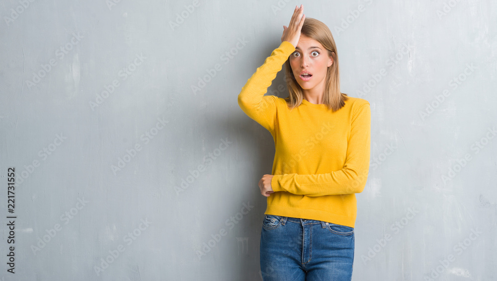Beautiful young woman standing over grunge grey wall surprised with hand on head for mistake, remember error. Forgot, bad memory concept.