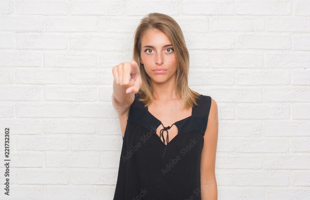 Beautiful young woman over white brick wall pointing with finger to the camera and to you, hand sign, positive and confident gesture from the front Beautiful young woman over white brick wall pointing with finger to the camera and to you, hand sign, positive and confident gesture from the front