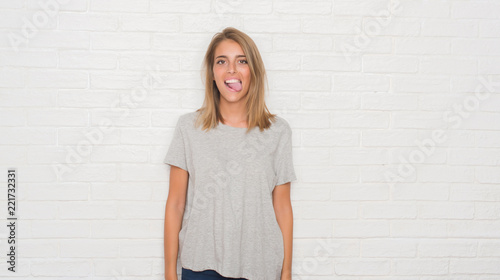 Beautiful young woman over white brick wall sticking tongue out happy with funny expression. Emotion concept. © Krakenimages.com