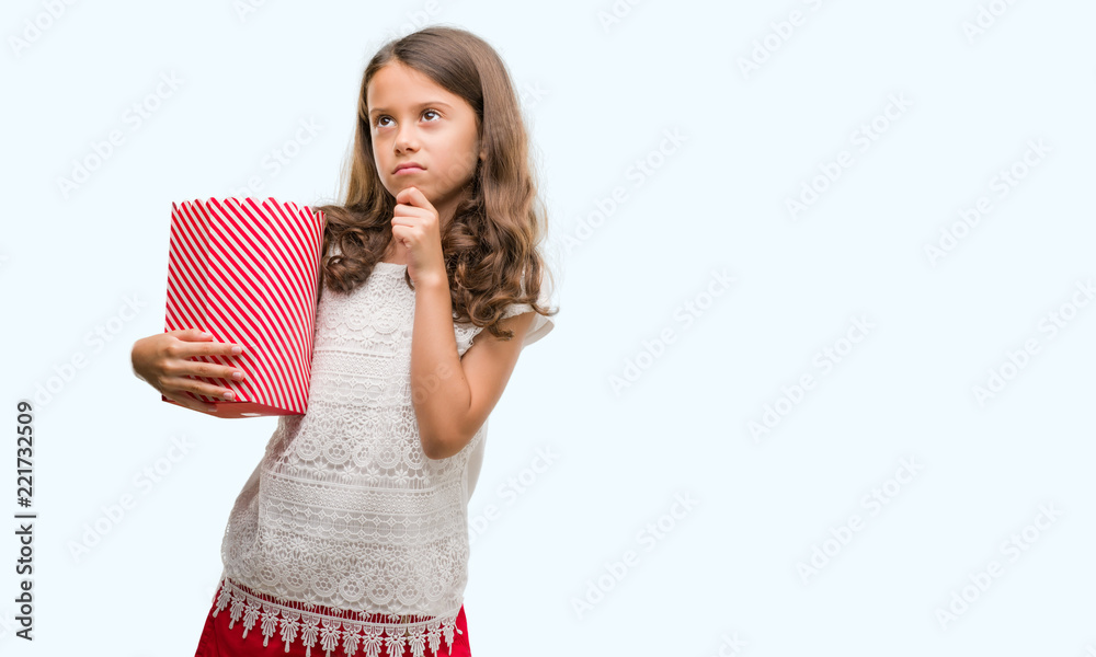 Brunette hispanic girl eating popcorn serious face thinking about question, very confused idea Brunette hispanic girl eating popcorn serious face thinking about question, very confused idea