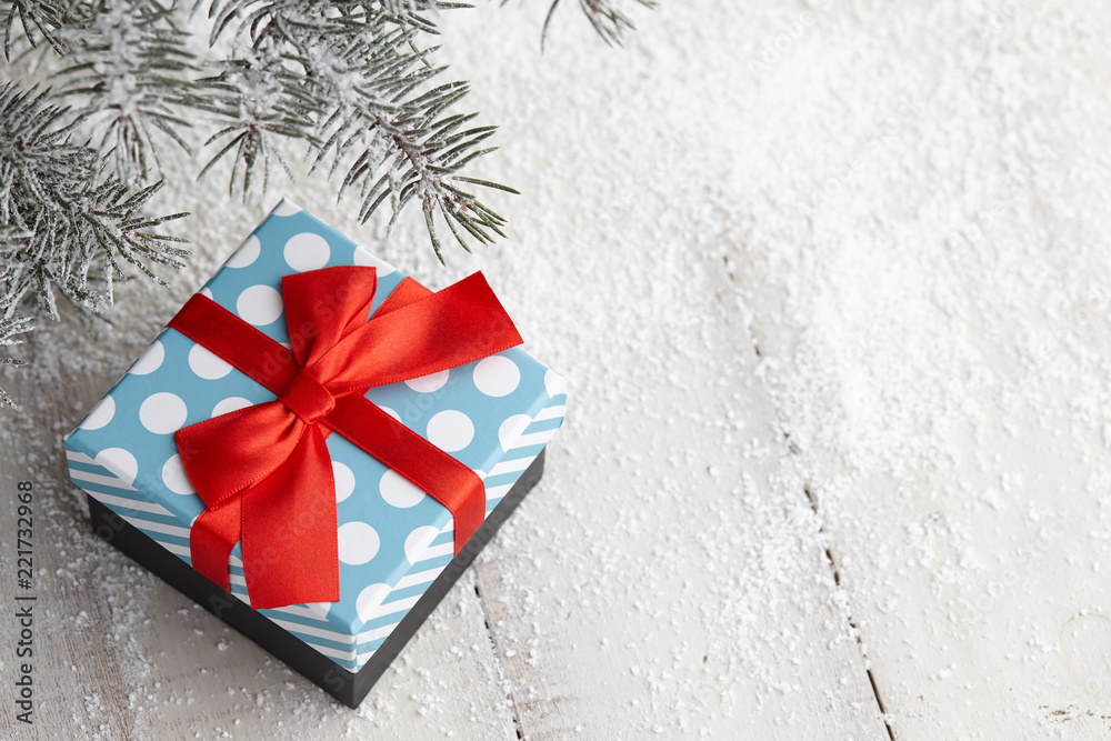 Christmas gift box with red ribbon bow under snowy fir tree