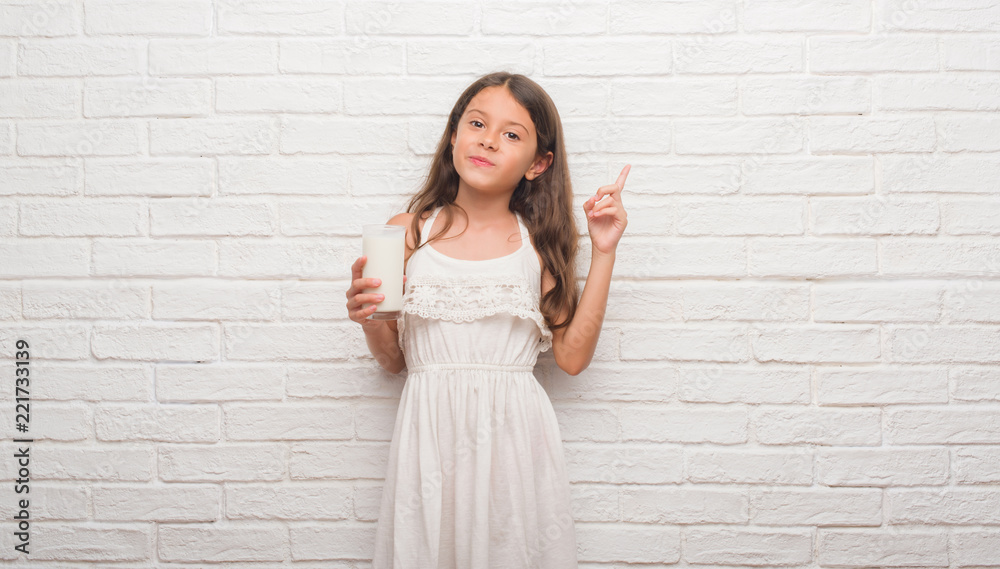Young hispanic kid over white brick wall drinking a glass of milk very happy pointing with hand and finger to the side Young hispanic kid over white brick wall drinking a glass of milk very happy pointing with hand and finger to the side