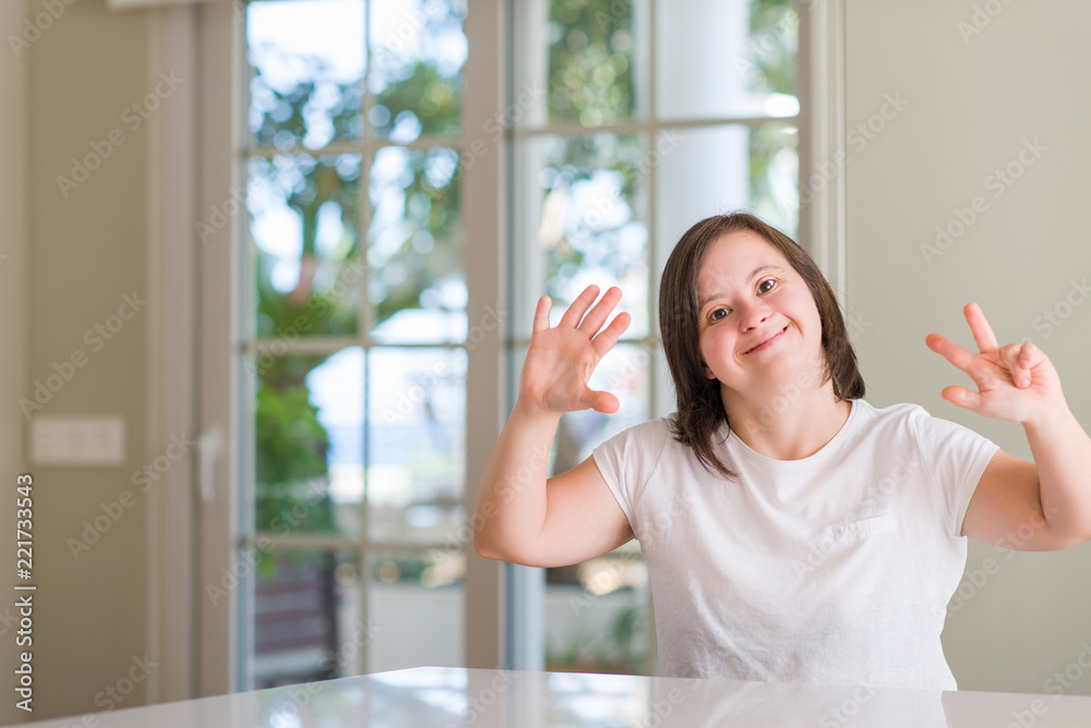 Down syndrome woman at home showing and pointing up with fingers number eight while smiling confident and happy.