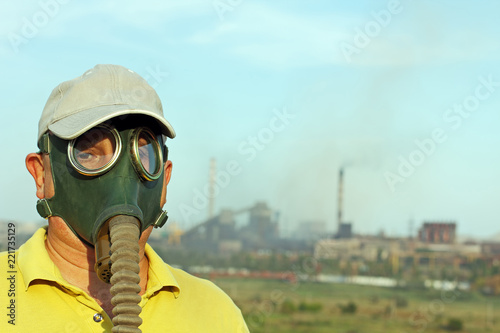 Men in gas mask looks at camera against the industrial factory and smoking pipes.