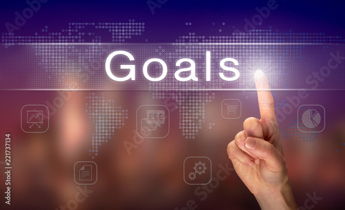 A hand selecting a Goals business concept on a clear screen with a colorful blurred background.