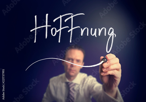 A businessman writing a Hope "Hoffnung" concept in German with a white pen on a clear screen.
