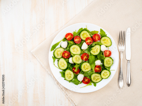 Fresh salad with tomatoes, cucumbers, arugula, mozzarella. Oil with spices, top view, white background, copy space
