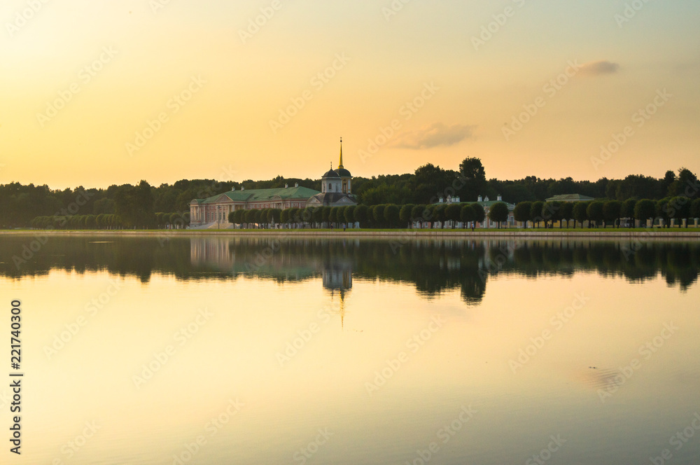 Summer sunset on the palace pond of museum-estate Kuskovo, Moscow. Russia. Mysterious moment when the orange sun says goodbye to nature. Its last reflection trembles on the water. 