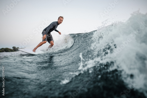 Man wakesurfing on the board down the blue water against the background of clear sky