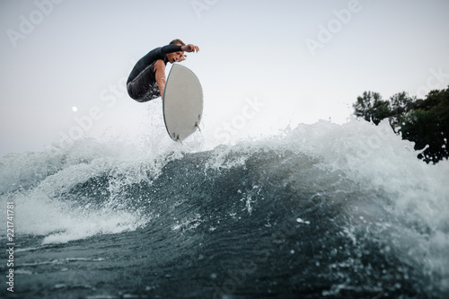 Photography Young and active wakeboarder jumping on the blue splashing wave against the back