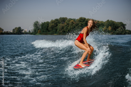 Beautiful blonde woman wakesurfer riding down the blue splashing wave