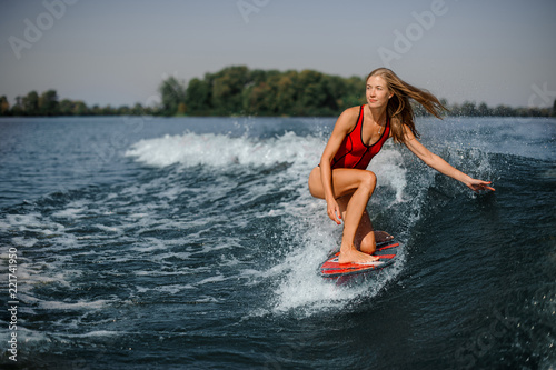 Attractive blonde woman wakesurfer riding down the blue splashing wave