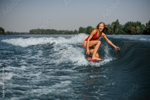 Happy blonde woman wakesurfer riding down the blue splashing wave